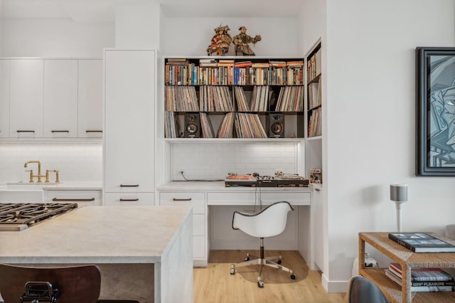 office with light wood-type flooring, built in desk, and sink