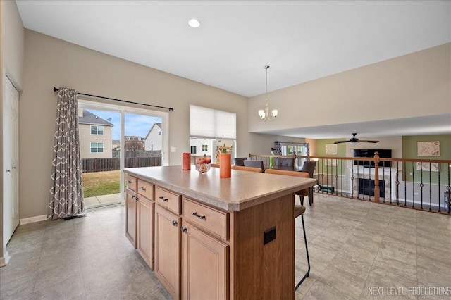 kitchen featuring ceiling fan with notable chandelier, a kitchen island, pendant lighting, and a kitchen breakfast bar