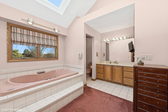 bathroom featuring tile patterned flooring, lofted ceiling with skylight, vanity, a relaxing tiled tub, and toilet