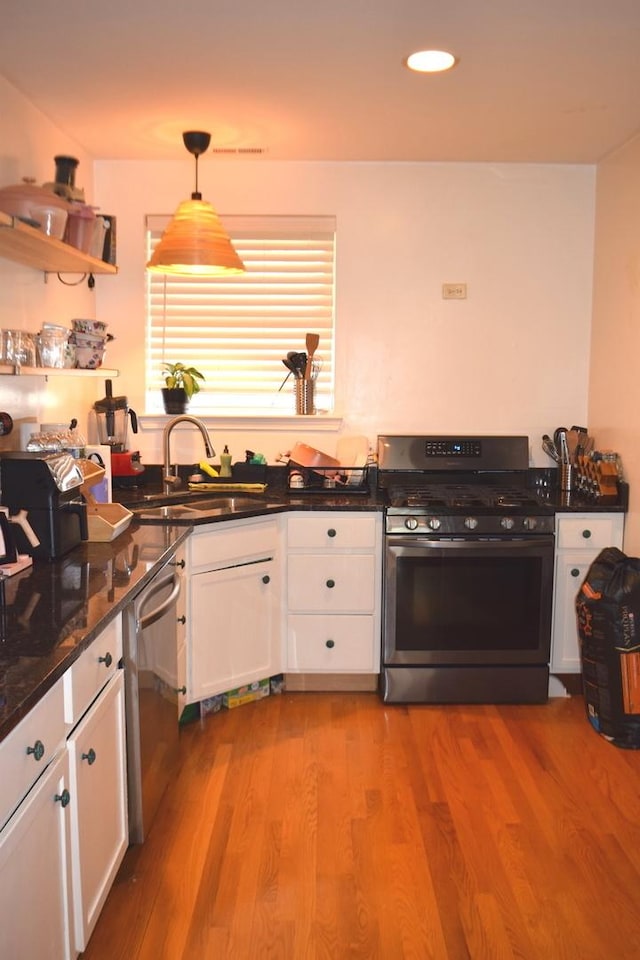 kitchen with appliances with stainless steel finishes, light hardwood / wood-style floors, white cabinetry, and decorative light fixtures