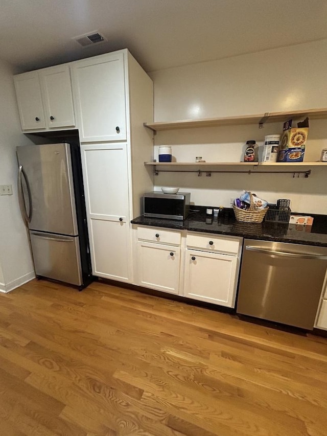 kitchen with light wood-type flooring, appliances with stainless steel finishes, dark stone countertops, and white cabinetry