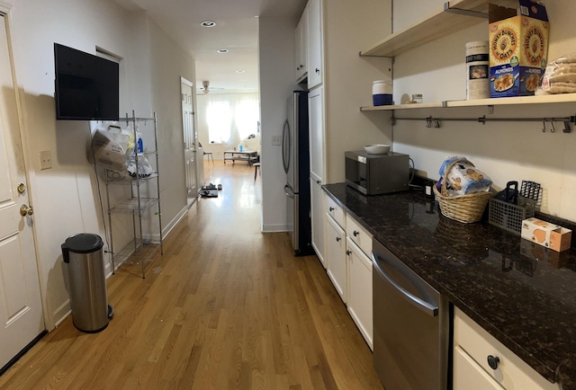 kitchen with light wood-type flooring, appliances with stainless steel finishes, white cabinets, and dark stone counters