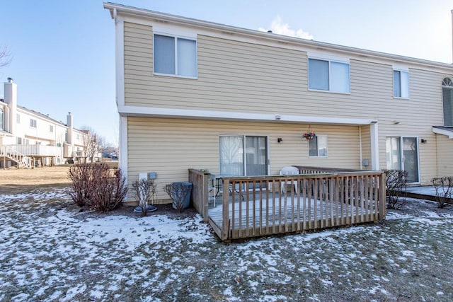 snow covered back of property with a wooden deck