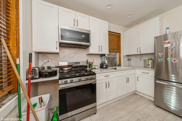 kitchen featuring sink, light tile patterned floors, appliances with stainless steel finishes, white cabinetry, and backsplash