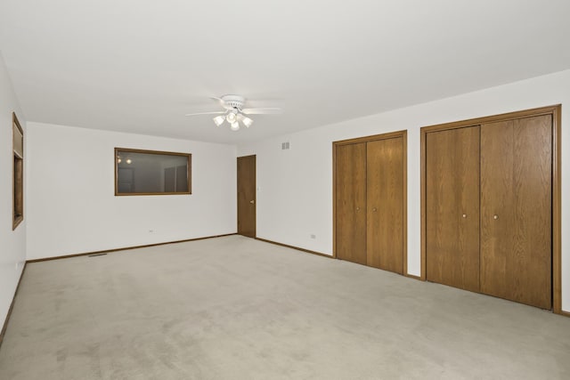 unfurnished bedroom featuring ceiling fan, light colored carpet, and multiple closets