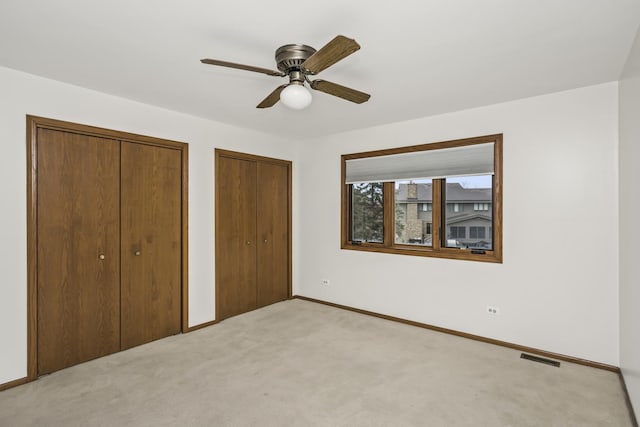 unfurnished bedroom with ceiling fan, light carpet, and two closets