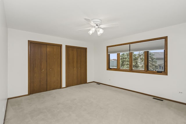 unfurnished bedroom featuring light carpet, ceiling fan, and multiple closets