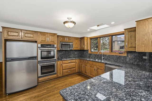 kitchen featuring stainless steel appliances, dark stone countertops, decorative backsplash, sink, and dark hardwood / wood-style floors