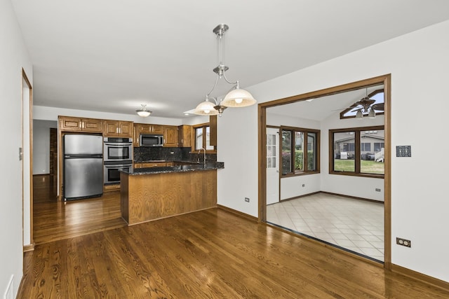 kitchen with appliances with stainless steel finishes, light hardwood / wood-style floors, backsplash, hanging light fixtures, and kitchen peninsula