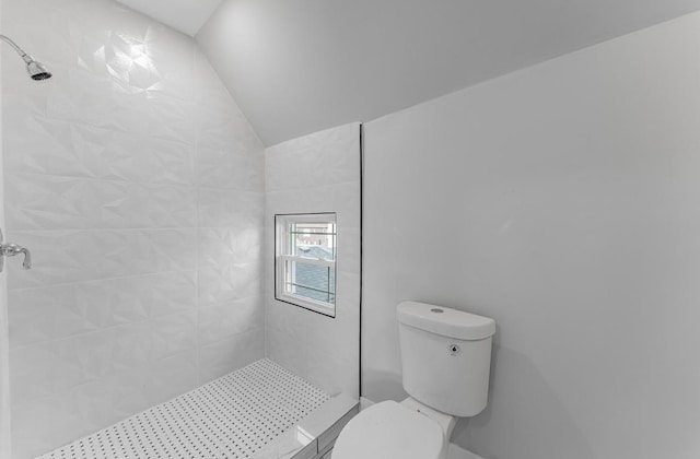 bathroom featuring tiled shower, toilet, and vaulted ceiling