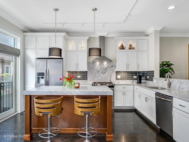 kitchen with pendant lighting, track lighting, appliances with stainless steel finishes, and wall chimney range hood