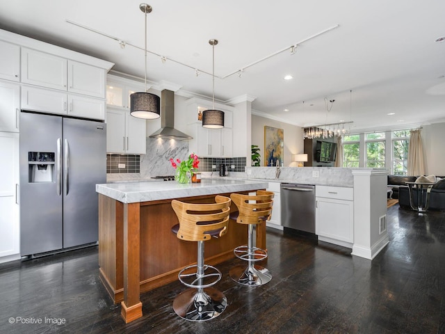 kitchen with rail lighting, appliances with stainless steel finishes, white cabinetry, kitchen peninsula, and wall chimney exhaust hood