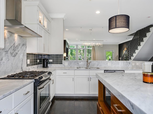 kitchen featuring sink, stainless steel gas stove, white cabinetry, hanging light fixtures, and wall chimney range hood