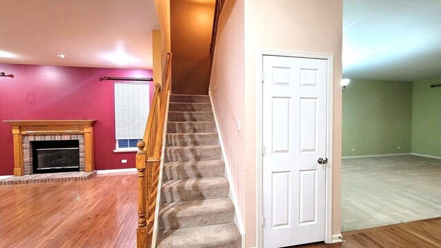 staircase with wood-type flooring and a brick fireplace