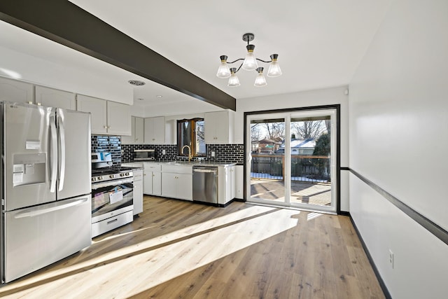 kitchen featuring white cabinets, appliances with stainless steel finishes, decorative light fixtures, a notable chandelier, and light wood-type flooring