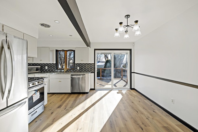 kitchen with decorative light fixtures, white cabinets, appliances with stainless steel finishes, and light hardwood / wood-style floors