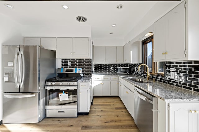 kitchen with appliances with stainless steel finishes, white cabinetry, sink, stone countertops, and light hardwood / wood-style flooring