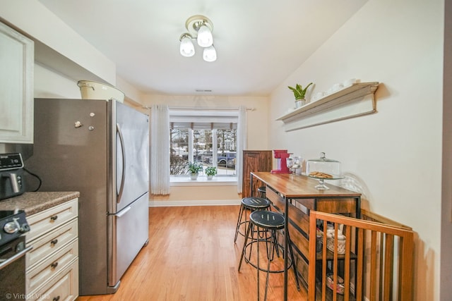 kitchen with stove, stainless steel refrigerator, and light hardwood / wood-style flooring