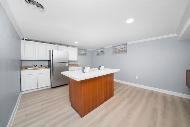 kitchen with white cabinets, a kitchen island, stainless steel fridge, ornamental molding, and light wood-type flooring