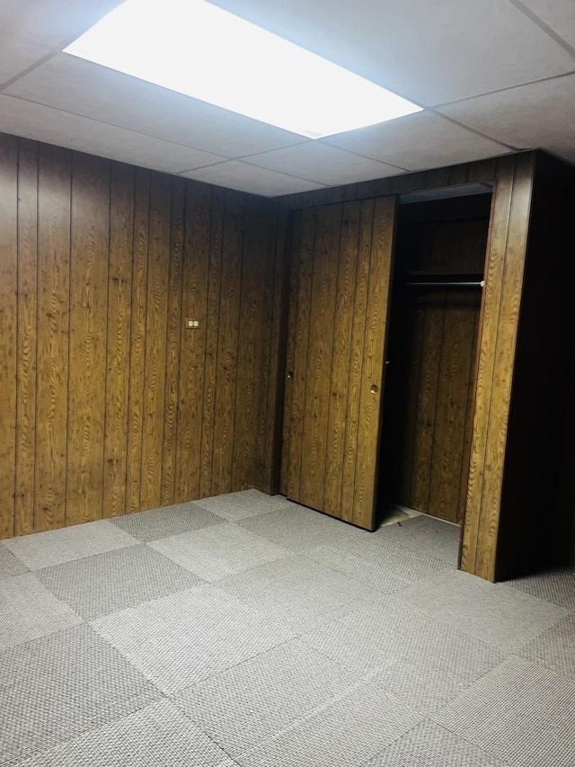 basement featuring light colored carpet, wooden walls, and a drop ceiling