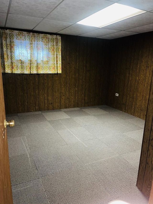 basement with a drop ceiling and wooden walls