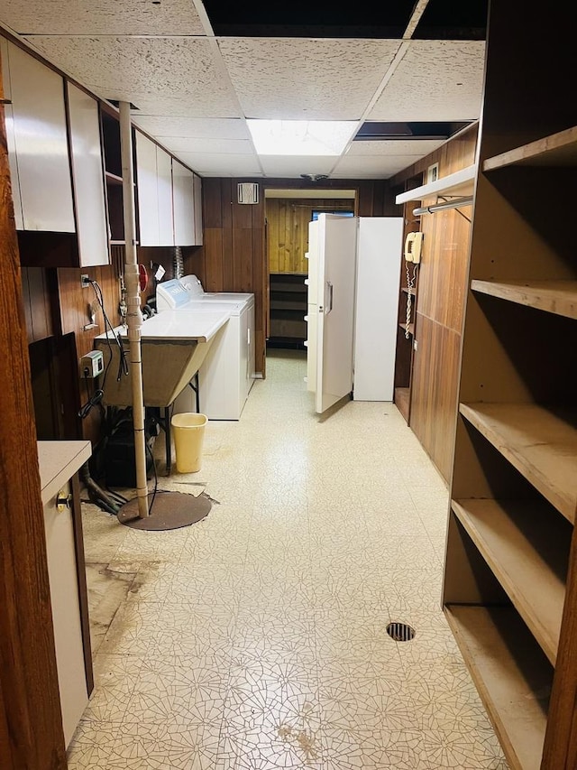 basement with washing machine and dryer, a drop ceiling, and wooden walls