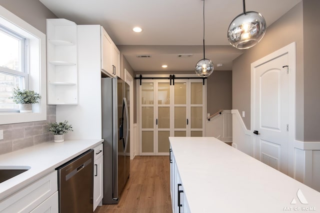 kitchen featuring light hardwood / wood-style floors, white cabinetry, a barn door, hanging light fixtures, and stainless steel appliances