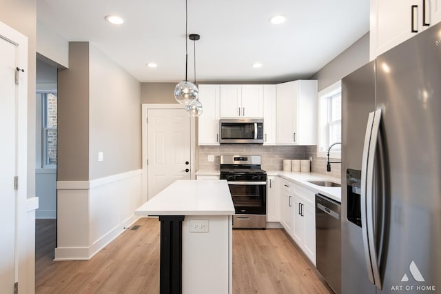 kitchen with white cabinetry, sink, a kitchen island, decorative light fixtures, and stainless steel appliances