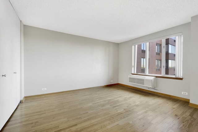 spare room with a textured ceiling, light hardwood / wood-style floors, and a wall mounted air conditioner