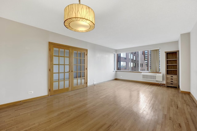 unfurnished living room with a wall mounted AC, wood-type flooring, and french doors