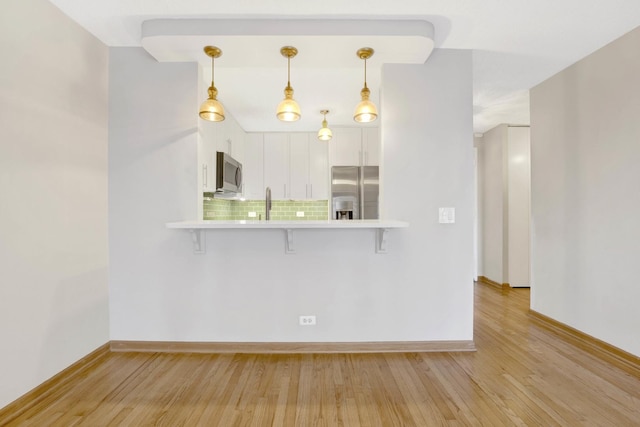 kitchen featuring a kitchen breakfast bar, kitchen peninsula, stainless steel appliances, and white cabinets