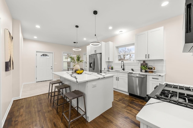 kitchen featuring stainless steel appliances, white cabinetry, decorative light fixtures, and a center island