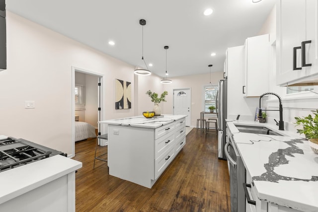 kitchen featuring white cabinetry, stainless steel appliances, a center island, decorative light fixtures, and sink