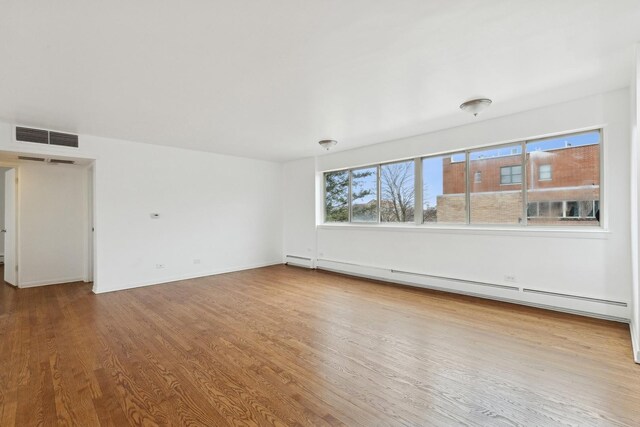 spare room featuring wood-type flooring and a baseboard heating unit