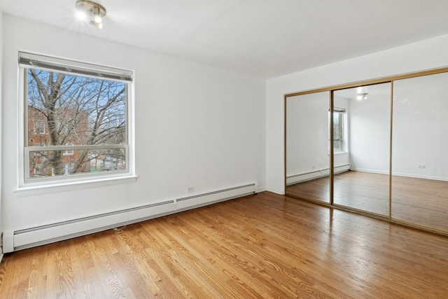 unfurnished bedroom featuring a baseboard heating unit, light hardwood / wood-style floors, and a closet