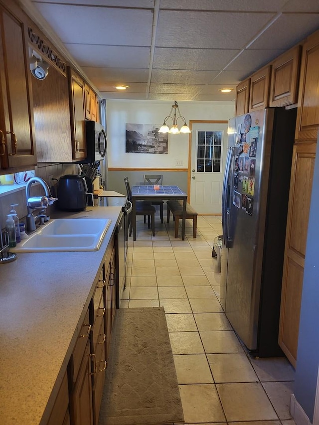 kitchen with sink, hanging light fixtures, light tile patterned floors, appliances with stainless steel finishes, and a drop ceiling