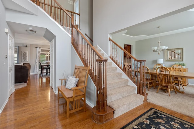 stairway with a high ceiling, hardwood / wood-style floors, and a notable chandelier