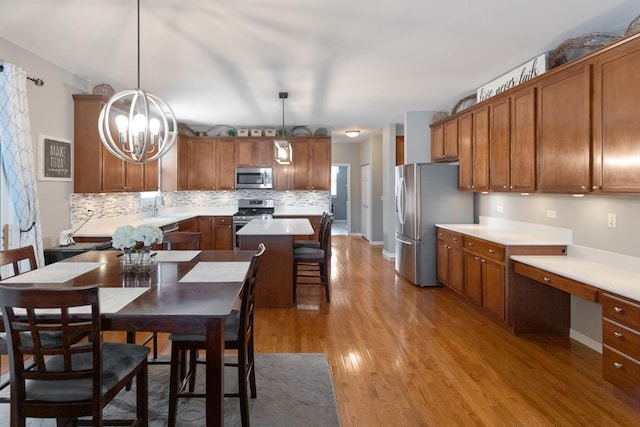 kitchen with pendant lighting, stainless steel appliances, a center island, built in desk, and light hardwood / wood-style floors