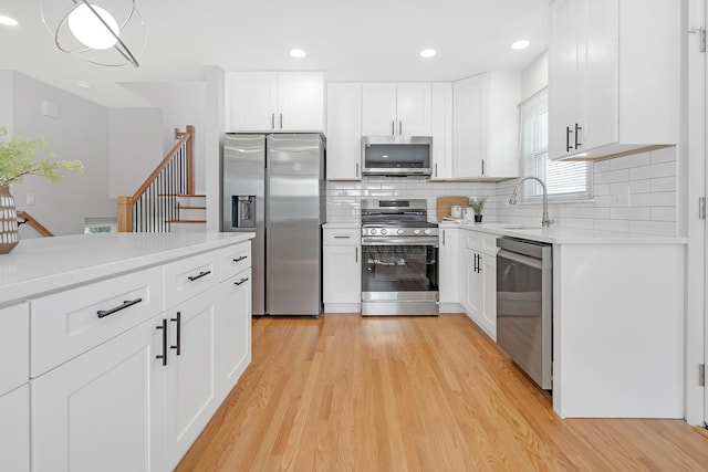 kitchen with white cabinetry, appliances with stainless steel finishes, backsplash, light hardwood / wood-style flooring, and sink