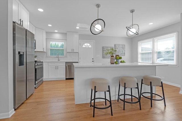 kitchen featuring stainless steel appliances, decorative backsplash, decorative light fixtures, white cabinets, and a center island