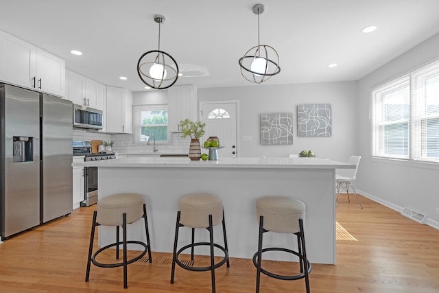 kitchen with appliances with stainless steel finishes, white cabinetry, and decorative light fixtures