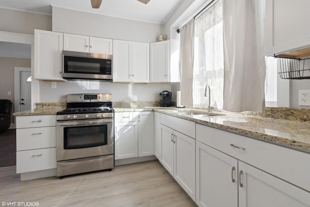 kitchen with light wood finished floors, appliances with stainless steel finishes, light stone counters, white cabinetry, and a sink