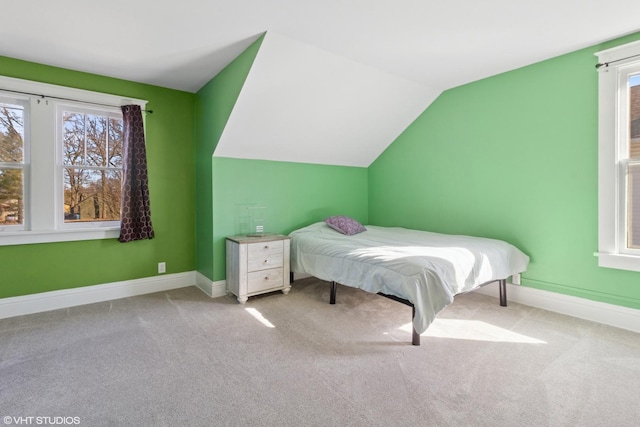 unfurnished bedroom featuring carpet, multiple windows, baseboards, and vaulted ceiling