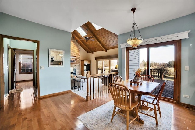 dining area with a skylight, wooden ceiling, a brick fireplace, light hardwood / wood-style flooring, and beamed ceiling