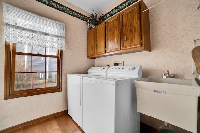 clothes washing area with a wealth of natural light, washer and clothes dryer, sink, and light hardwood / wood-style floors