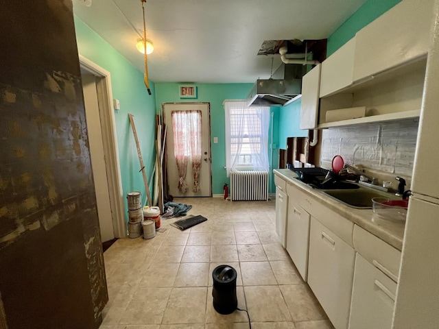 kitchen featuring sink, light tile patterned floors, radiator, white cabinets, and backsplash