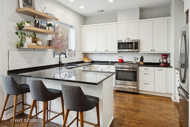 kitchen with white cabinetry, sink, dark hardwood / wood-style flooring, kitchen peninsula, and stainless steel appliances