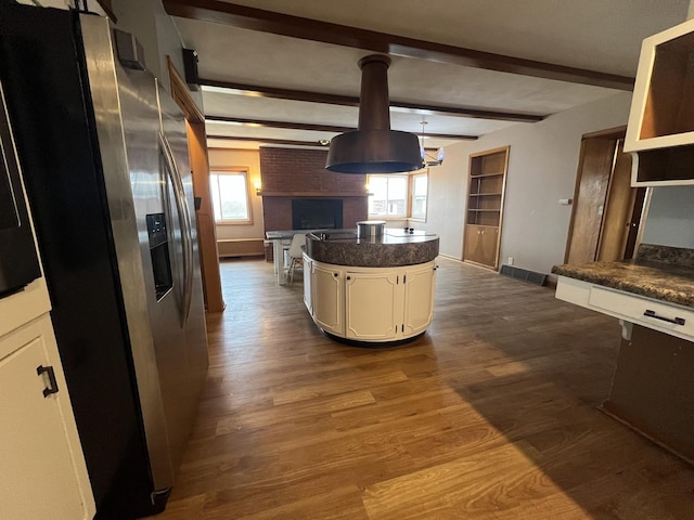 kitchen featuring dark wood-type flooring, stainless steel fridge, a kitchen island, a brick fireplace, and beamed ceiling