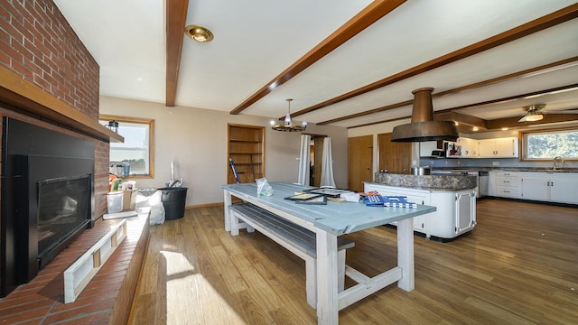 dining room featuring sink, beam ceiling, light hardwood / wood-style floors, and a brick fireplace