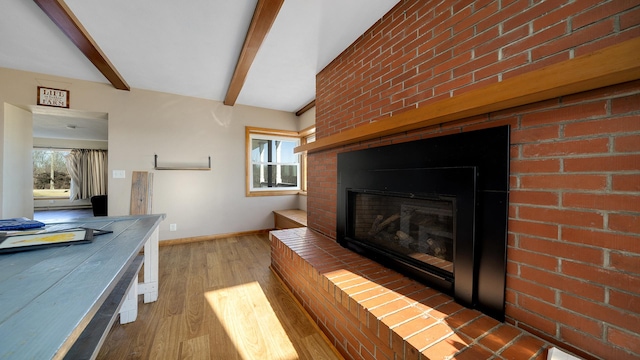 living room featuring brick wall, a wealth of natural light, beam ceiling, and light hardwood / wood-style floors